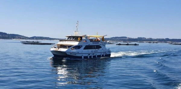 A white passenger ferry with "Restaurant" written on its side travels through calm blue water on a sunny day. Hills are in the distance.