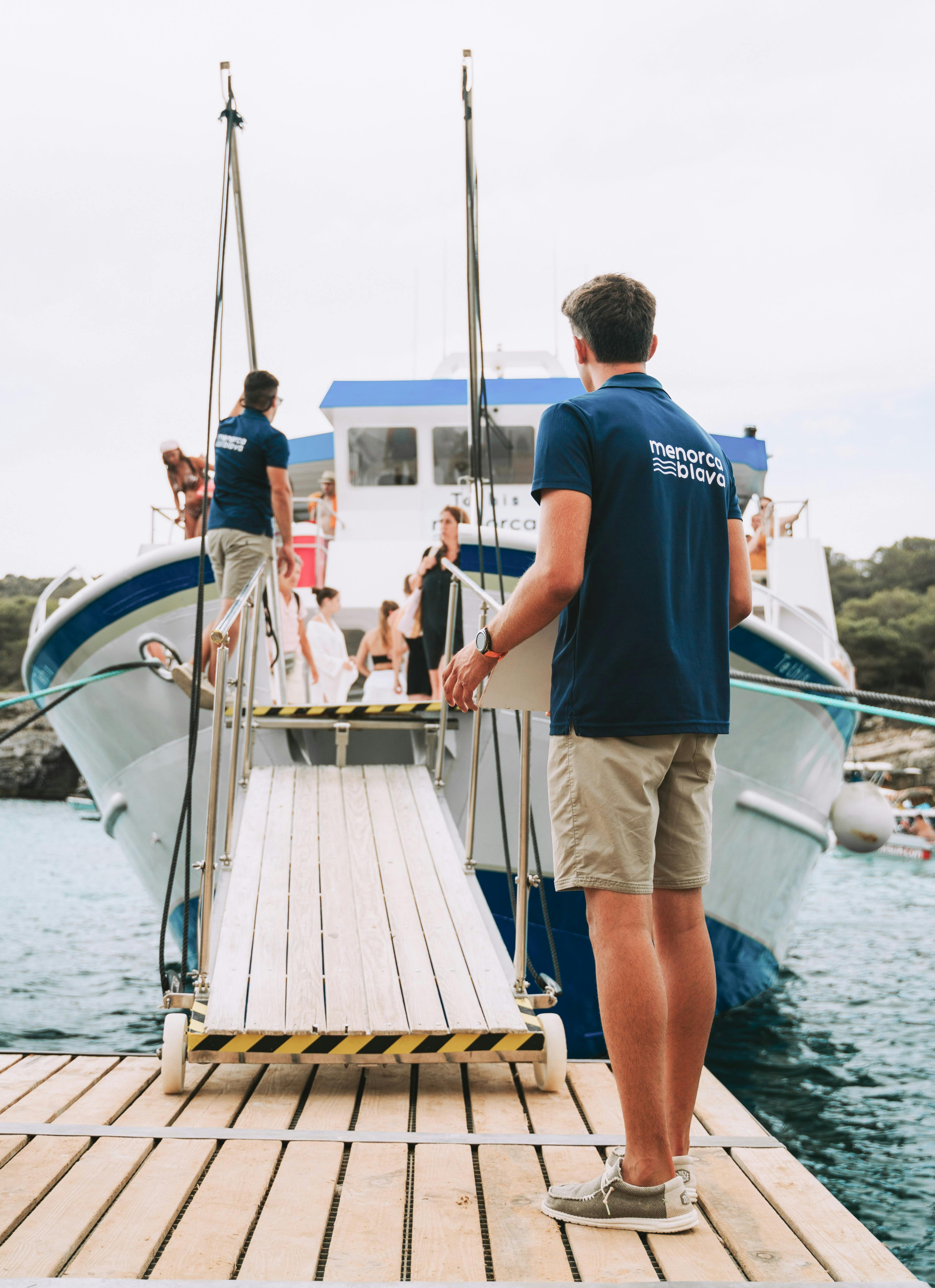 A boat labelled 'Menorca Blava' partially submerged, with visible water and a blurred shoreline in the background.