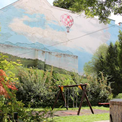 Urban väggmålning av landsbygden med luftballong, grönska, en lekplatsgunga och två barn i hörnet.