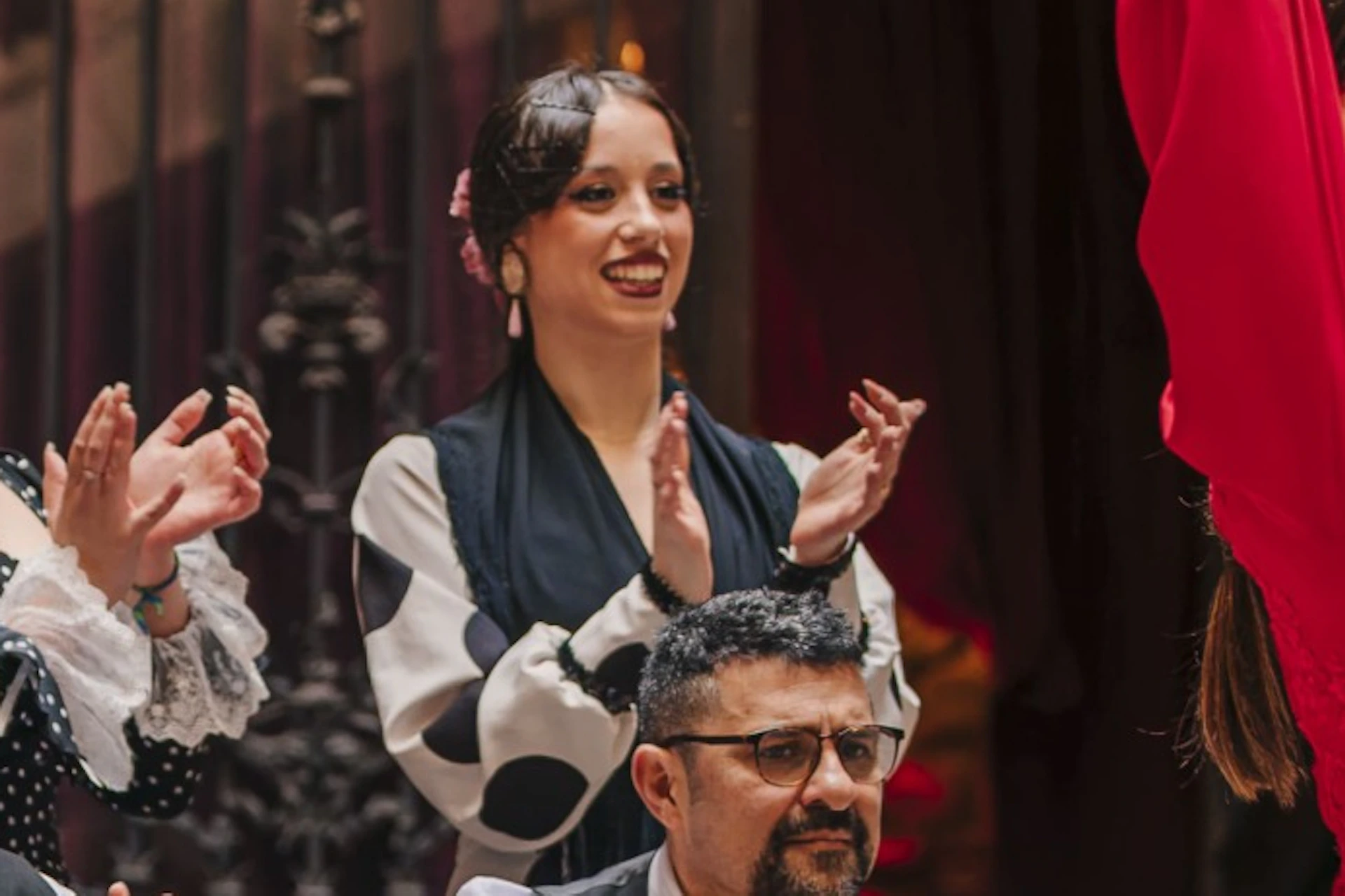 Two dancers performing a flamenco dance in a courtyard with musicians seated behind them, playing guitar and clapping.