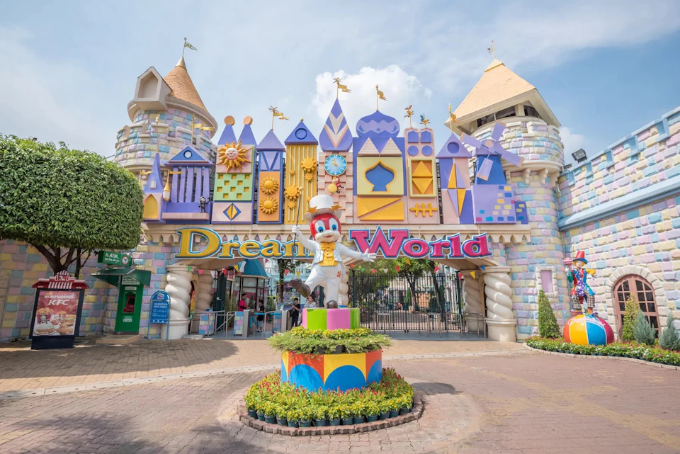 Colorful, castle-themed amusement park entrance with "Dream World" sign and character statue, under a clear blue sky.