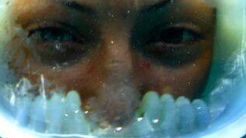 Person snorkeling underwater wearing a full-face mask, with clear blue water surrounding them.