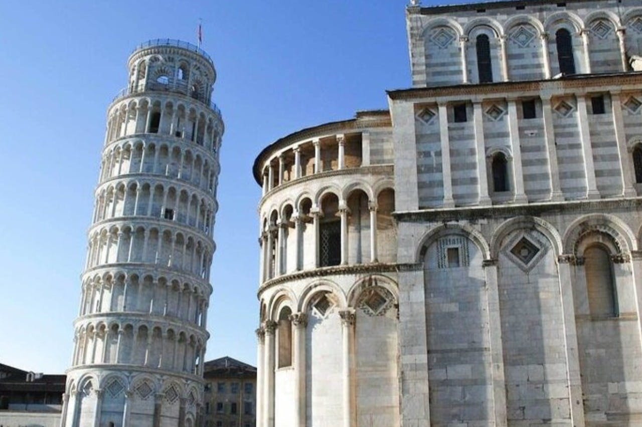 Ο Κεκλιμένος Πύργος της Πίζας και ο παρακείμενος καθεδρικός ναός κάτω από έναν καταγάλανο ουρανό.