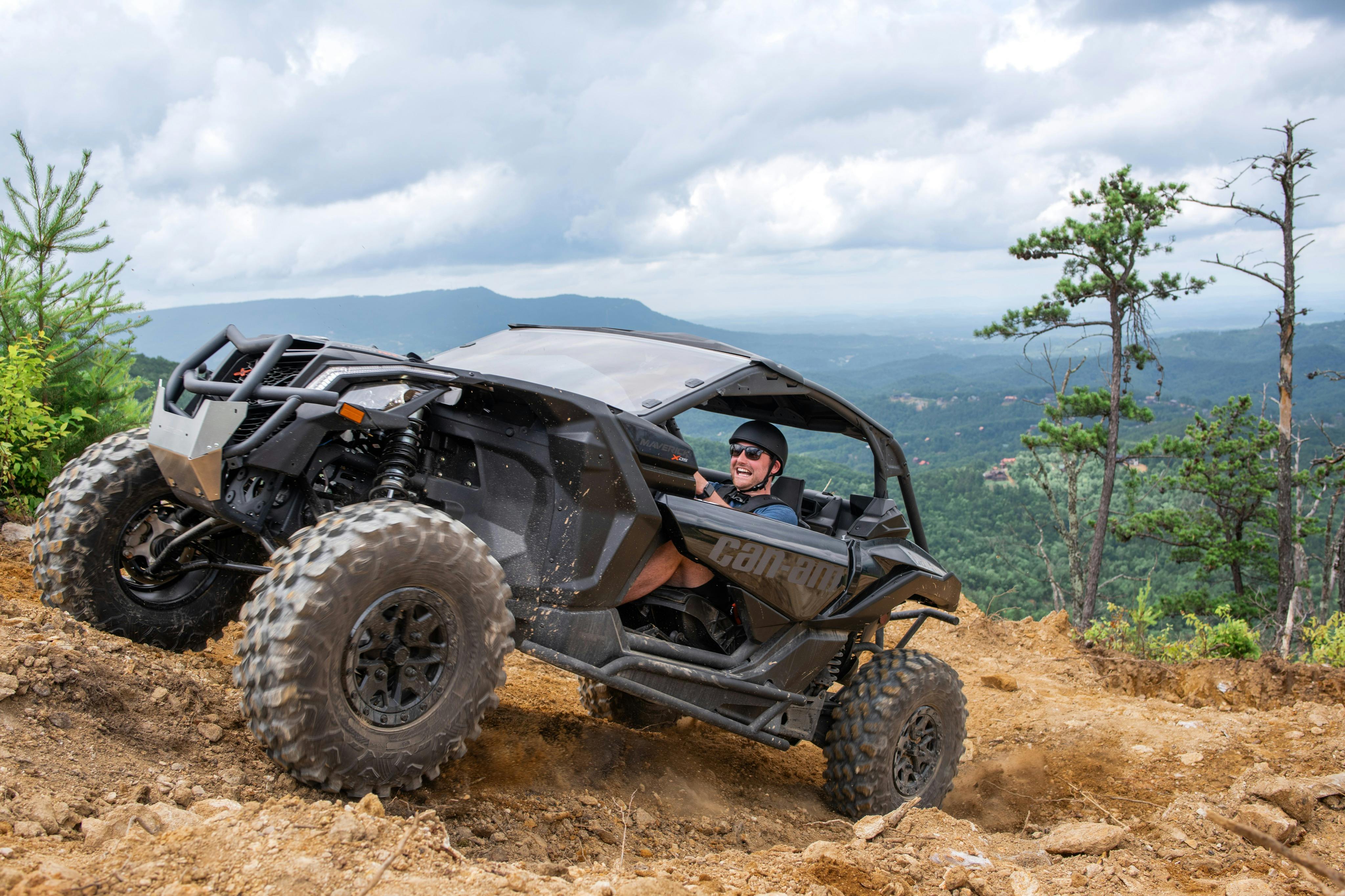風光明媚な山と森の景色を背景に、ダートトレイルでオフロード車を運転している人。