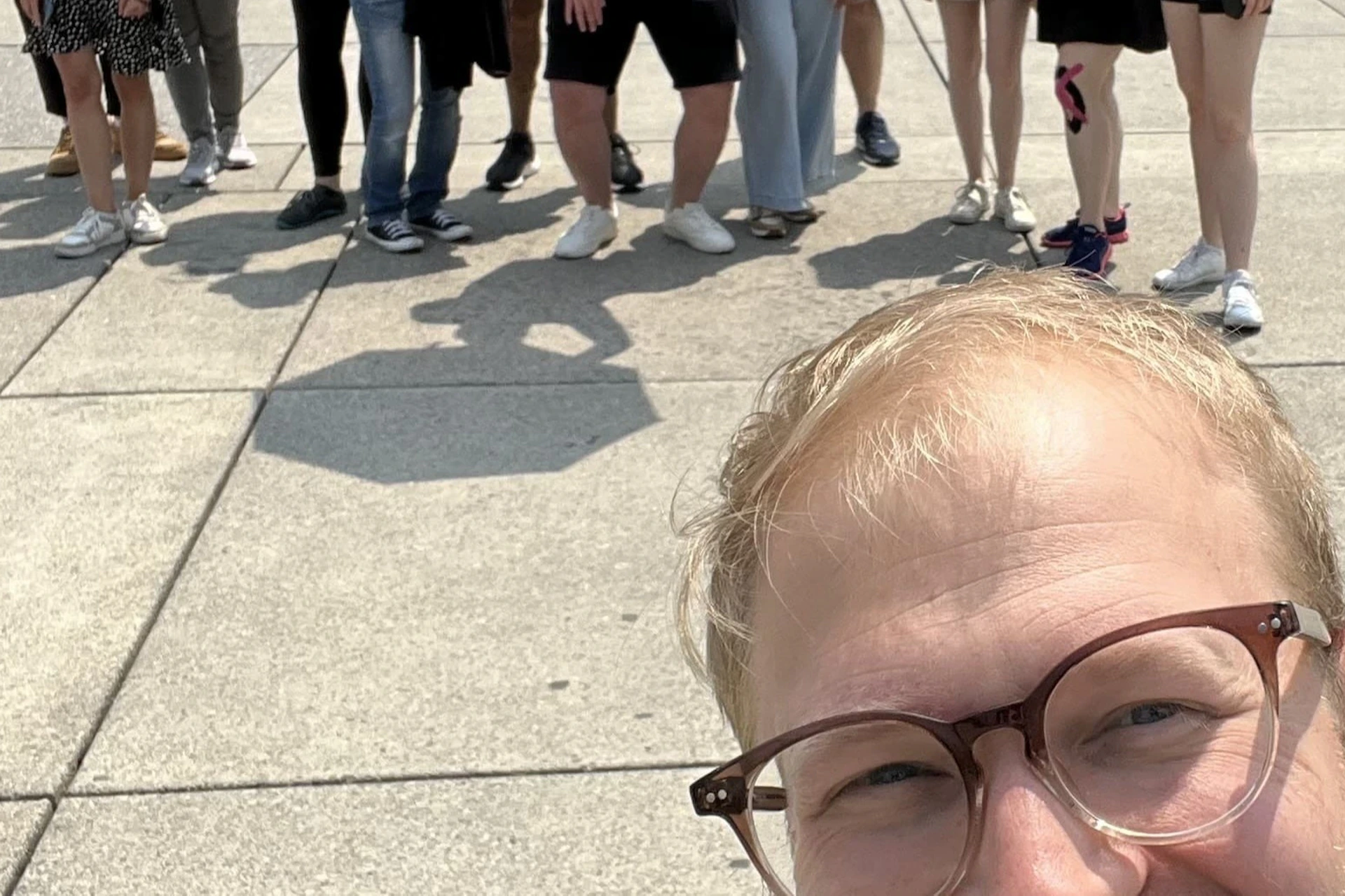 A group of people posing in front of large "Toronto" letters in a plaza, with one person in the foreground taking a selfie.