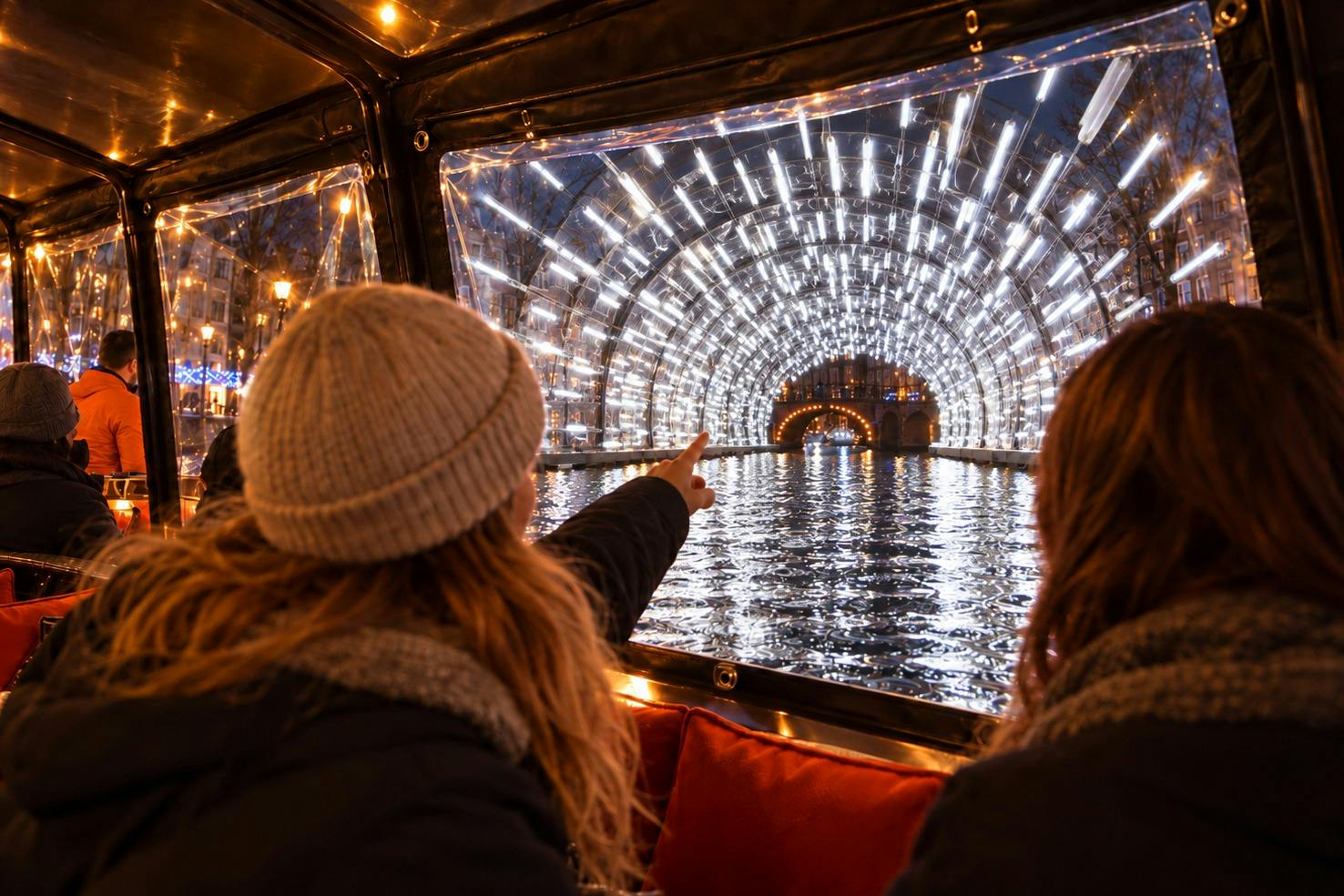 Two people seated on a boat admire a tunnel illuminated with bright lights reflecting on the water at night.