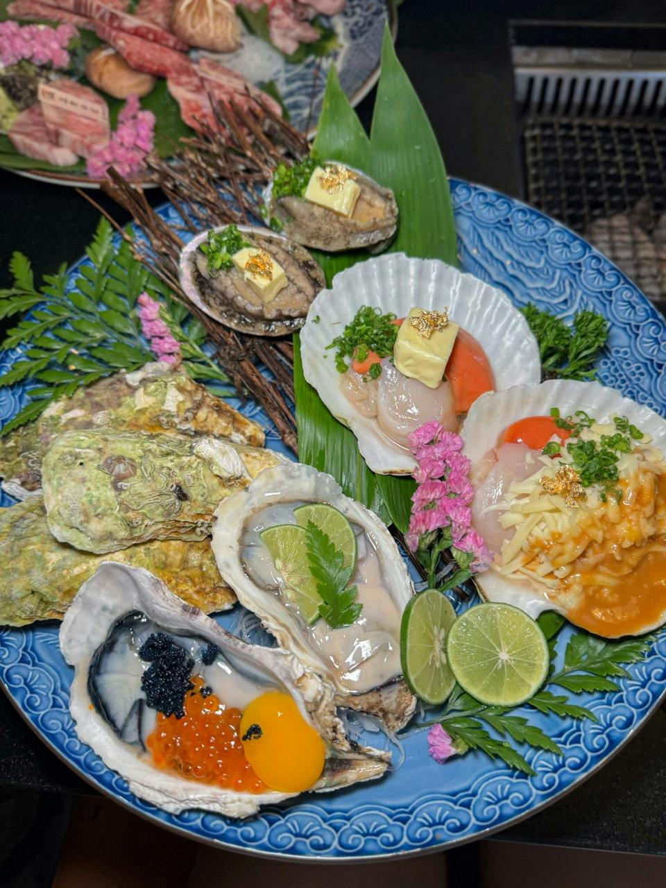 A plate of assorted seafood including oysters, scallops, and garnishes, presented with decorative flowers and lime slices.
