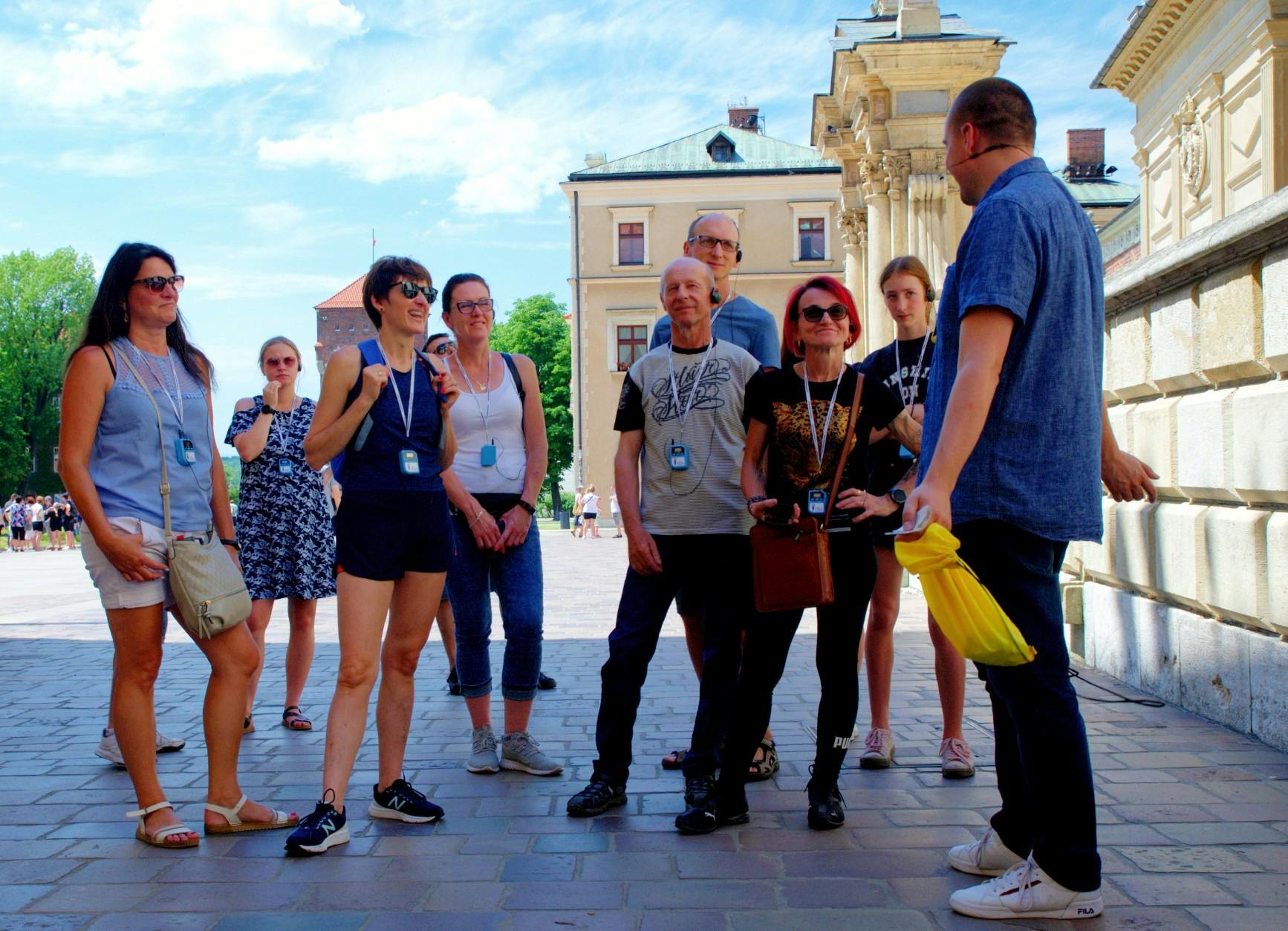 A group of people listening to a tour guide outside historical buildings under a partly cloudy sky.