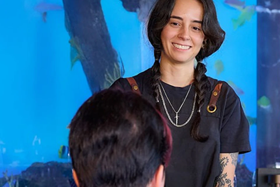 A restaurant with an aquarium backdrop. A server smiles while interacting with seated customers at a table.
