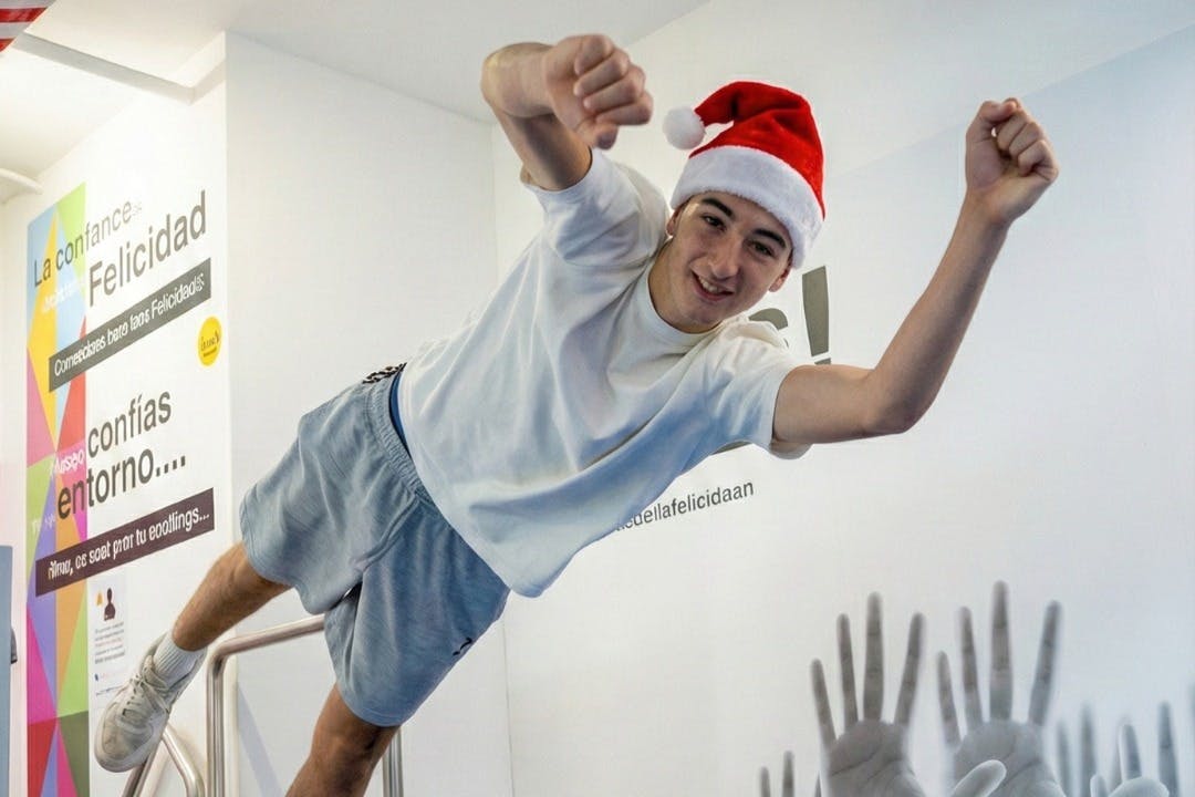 산타 모자를 쓰고 캐주얼한 옷을 입은 사람이 밝은 방에서 손을 들어 올린 것처럼 포즈를 취하고 있습니다.