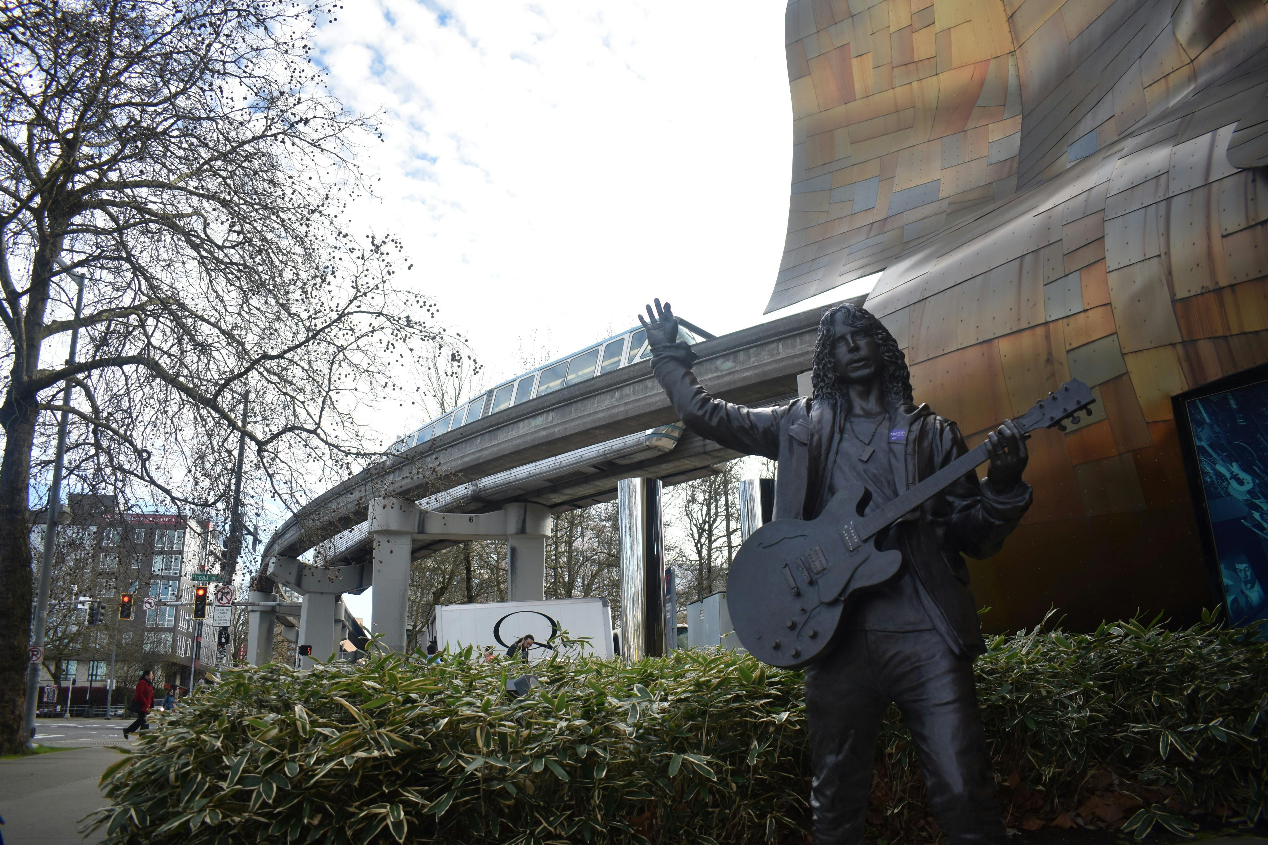モダンな建物と木々のそばにある、高架モノレールトラックを背景にしたギターを持った男性の像。