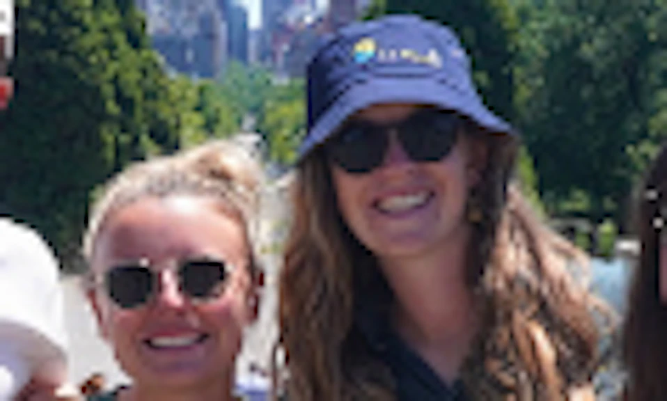 Four people pose together in front of a park with a city skyline in the background on a sunny day.