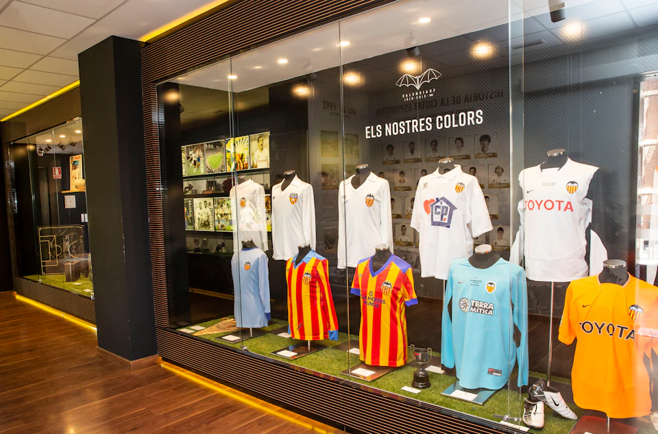 Display case with various Valencia CF football jerseys on mannequins, along with trophies, in a well-lit exhibit.