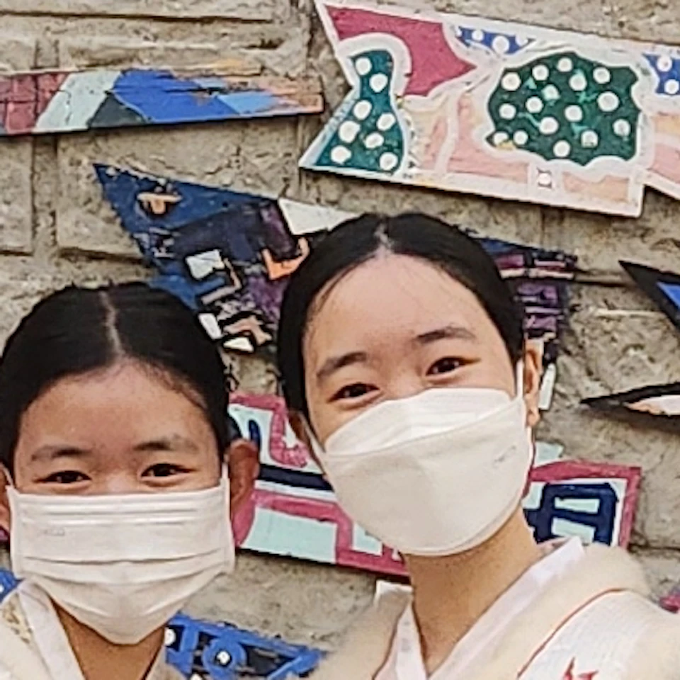 A group of four people in traditional attire standing in front of a wall decorated with colorful wooden plaques.