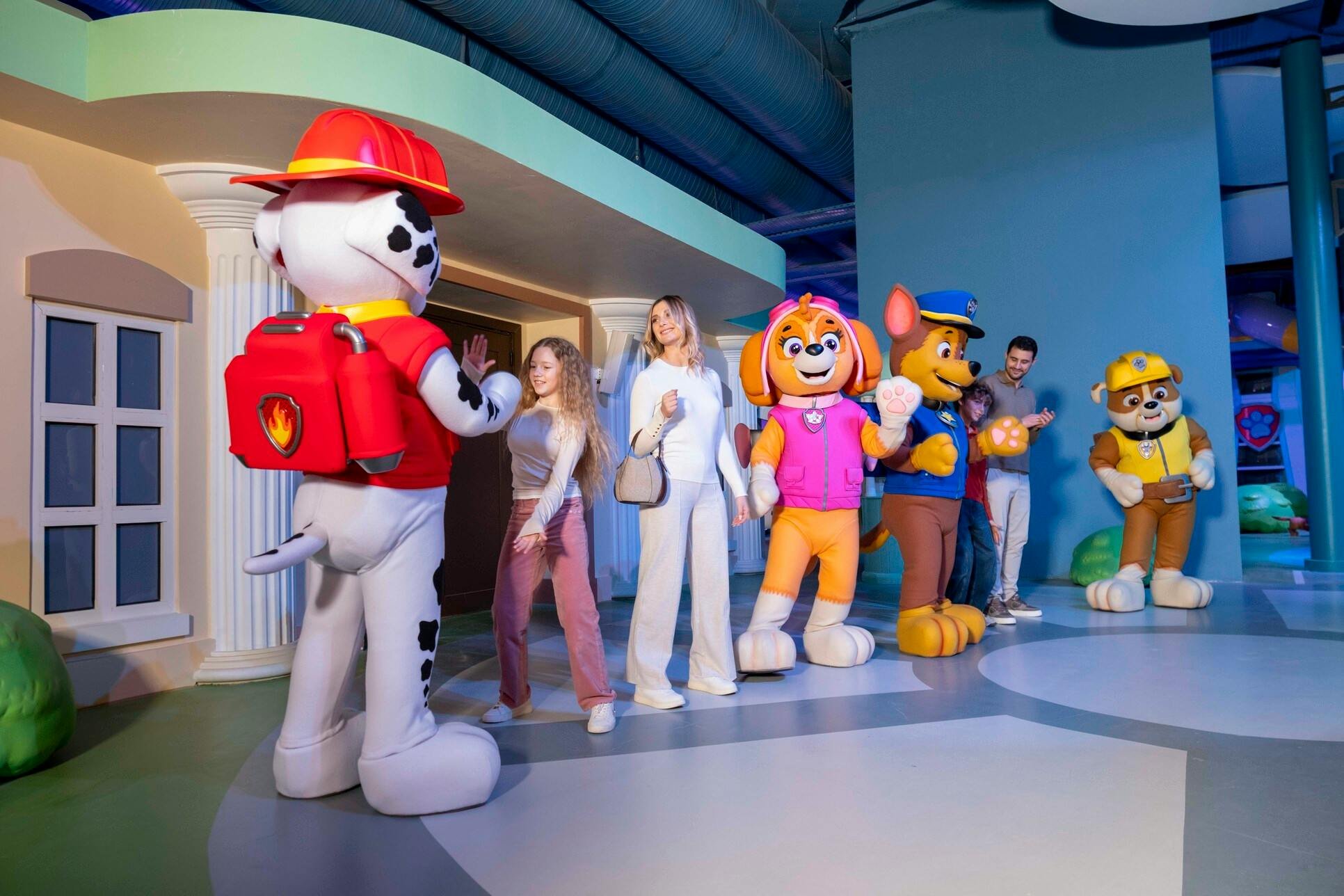 Mensen in interactie met mascottes op menselijke grootte van stripfiguren in een gethematiseerde binnenomgeving met kleurrijke achtergronden.