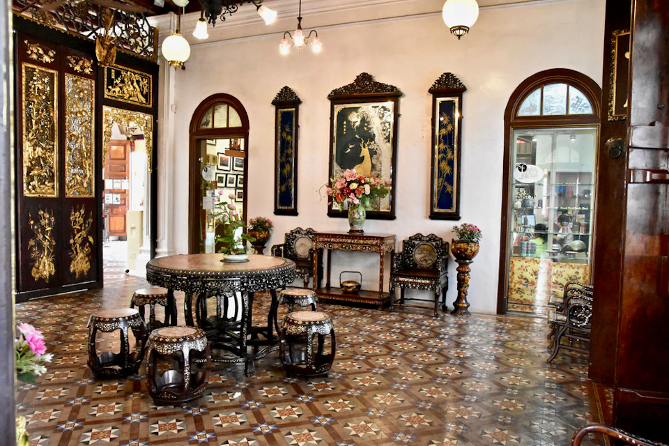 An ornate room with antique furniture, including a round table with stools, decorative vases, framed wall art, and arched doorways.