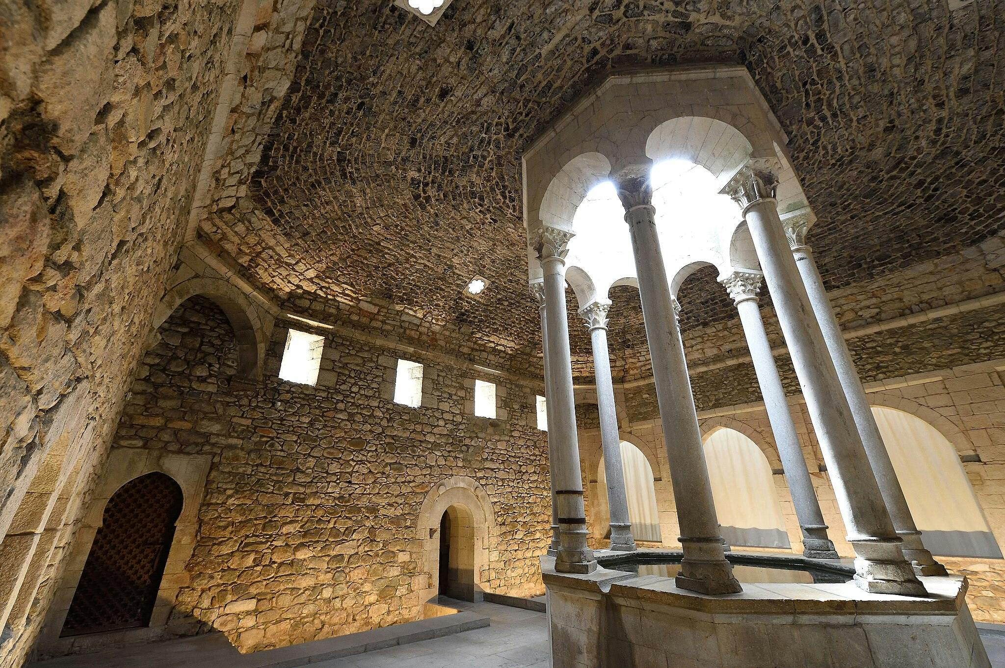 Stone-walled room with arched doorways, a high domed ceiling, and a central structure supported by slender columns.