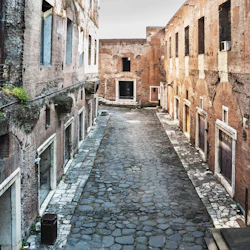 En kullerstensgata omgiven av gamla tegelbyggnader med välvda dörröppningar och några små växter som växer på väggarna.