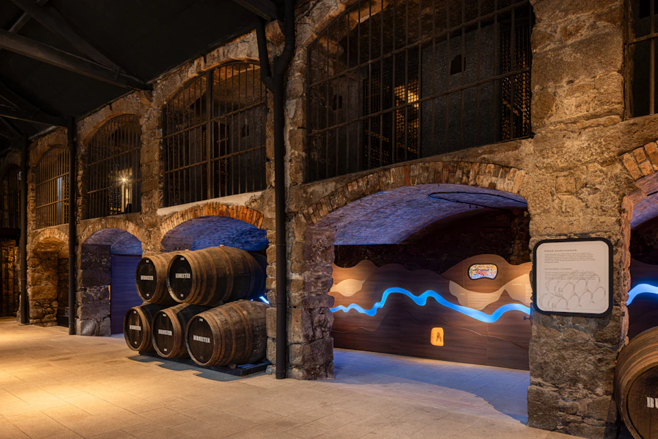 A rustic interior with stone walls, barrels stacked on the left, and a glowing blue wave design on a wooden panel on the right.