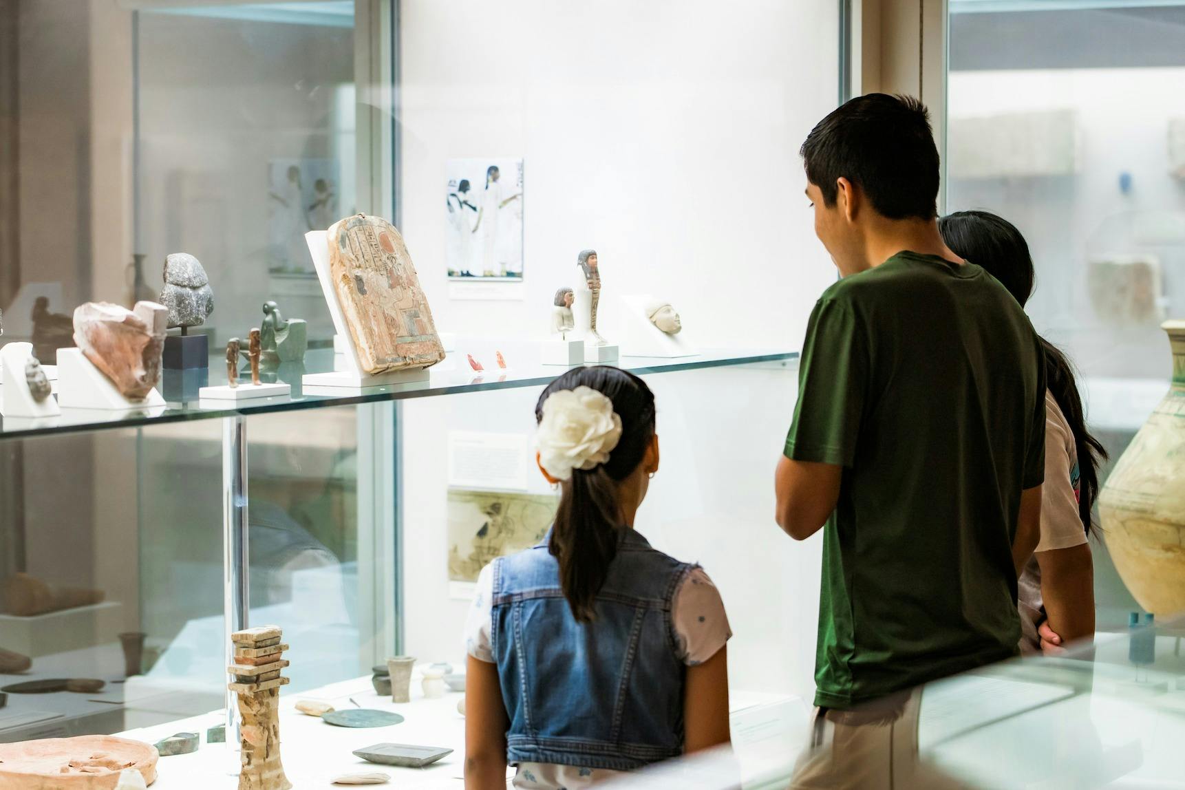 Drie mensen, op de rug gezien, bekijken oude artefacten in een glazen vitrine in een museum.