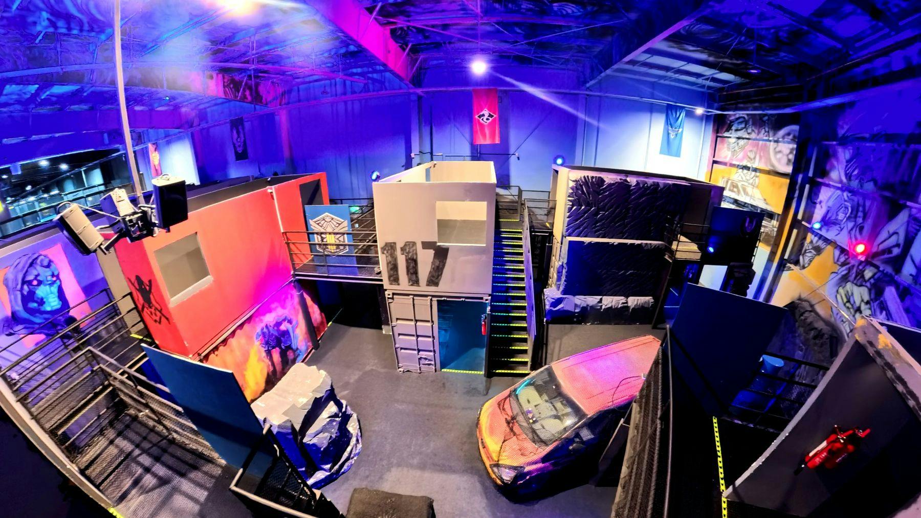 Εσωτερική αρένα ετικετών λέιζερ με πολύχρωμο φωτισμό, με εμπόδια όπως τοίχους, αυτοκίνητο και σκάλα με την ένδειξη «117».