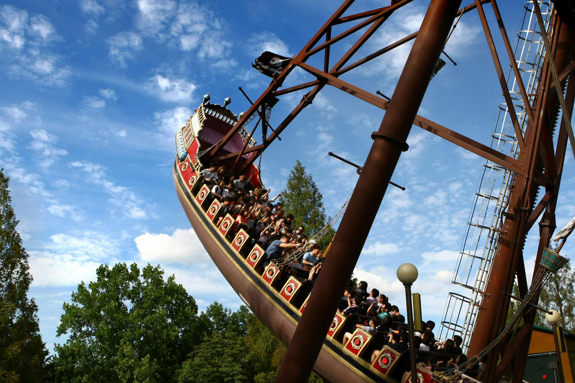 Persone che cavalcano una nave pirata oscillante sullo sfondo di alberi e di un cielo azzurro parzialmente nuvoloso.