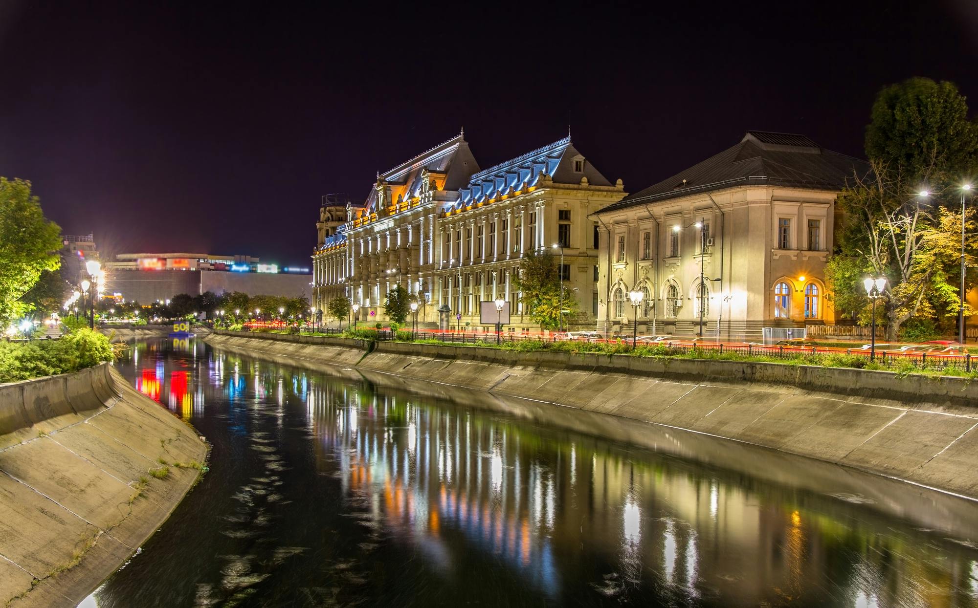 Historic buildings with illuminated facades along a riverside at night, reflecting on the calm water.