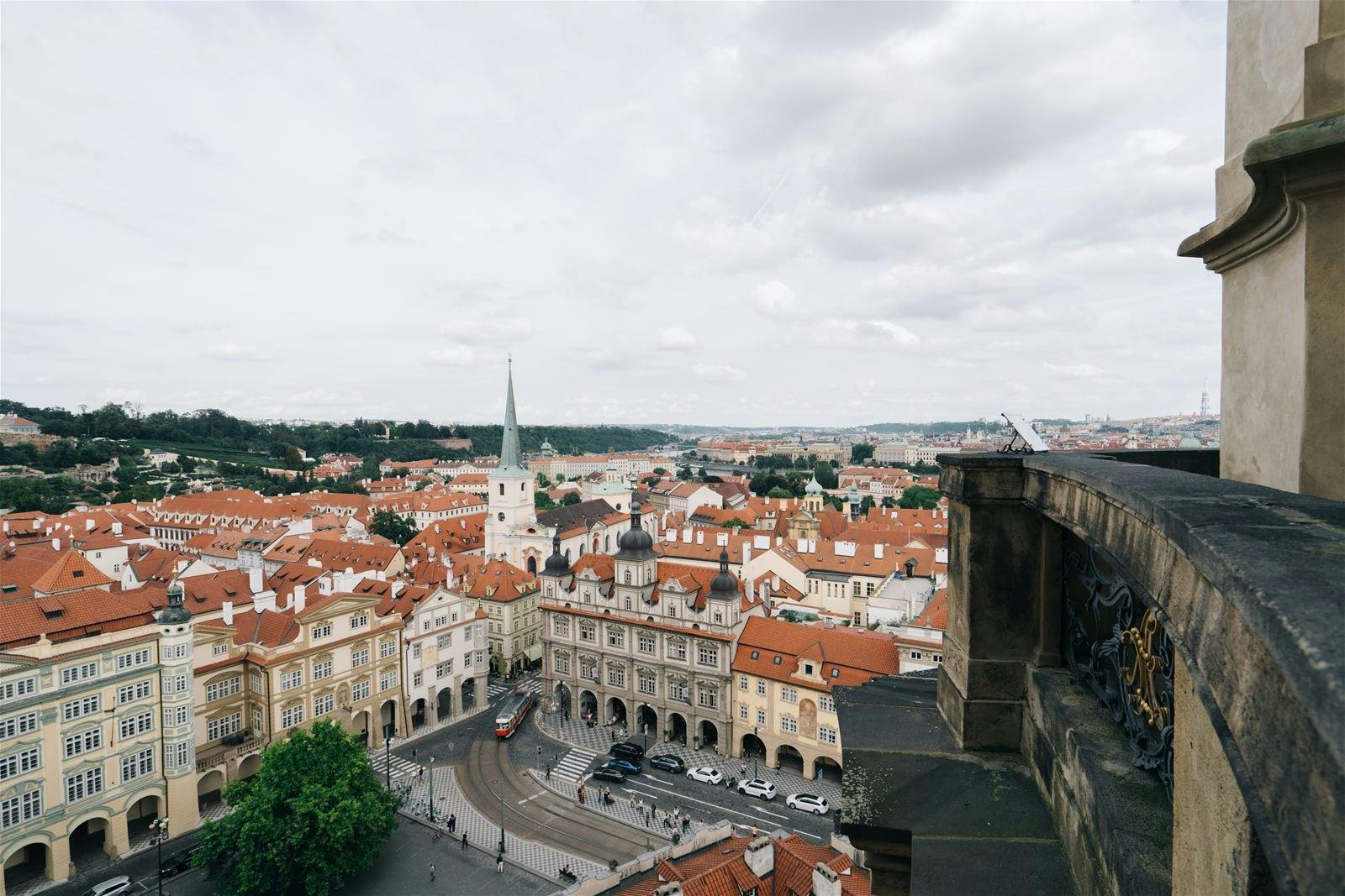 Udsigt over en europæisk by med røde tegltage, en kirke med et højt spir og biler på en brostensbelagt gade.