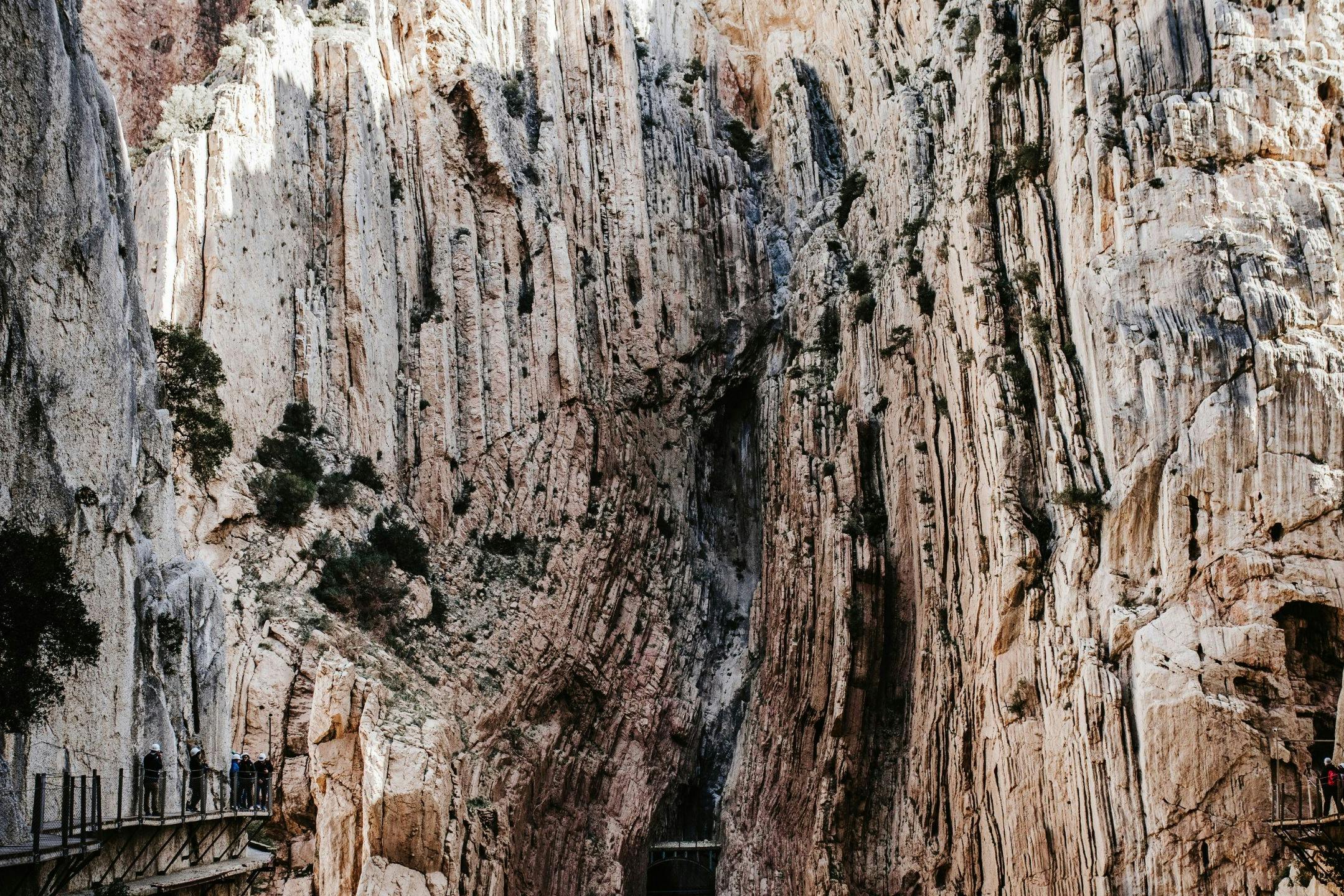 Tall, rugged cliffs with a group of people standing on a narrow ledge in the lower-left corner.