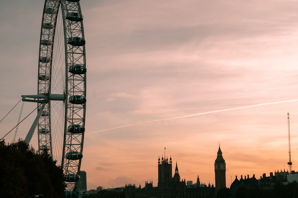 Ferris wheel and Gothic-style buildings, including Big Ben, silhouetted against a pink and orange sunset sky.