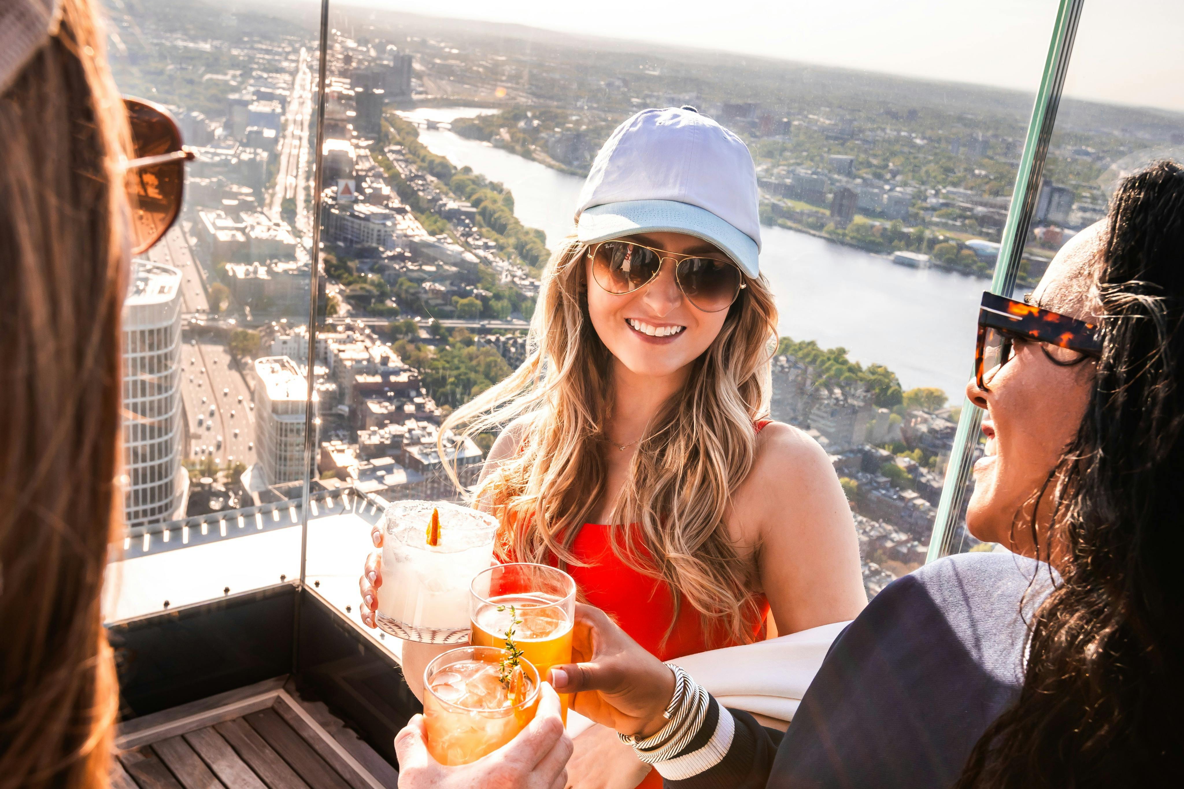 Due persone che brindano con un cocktail su un tetto con un paesaggio urbano e un fiume sullo sfondo.