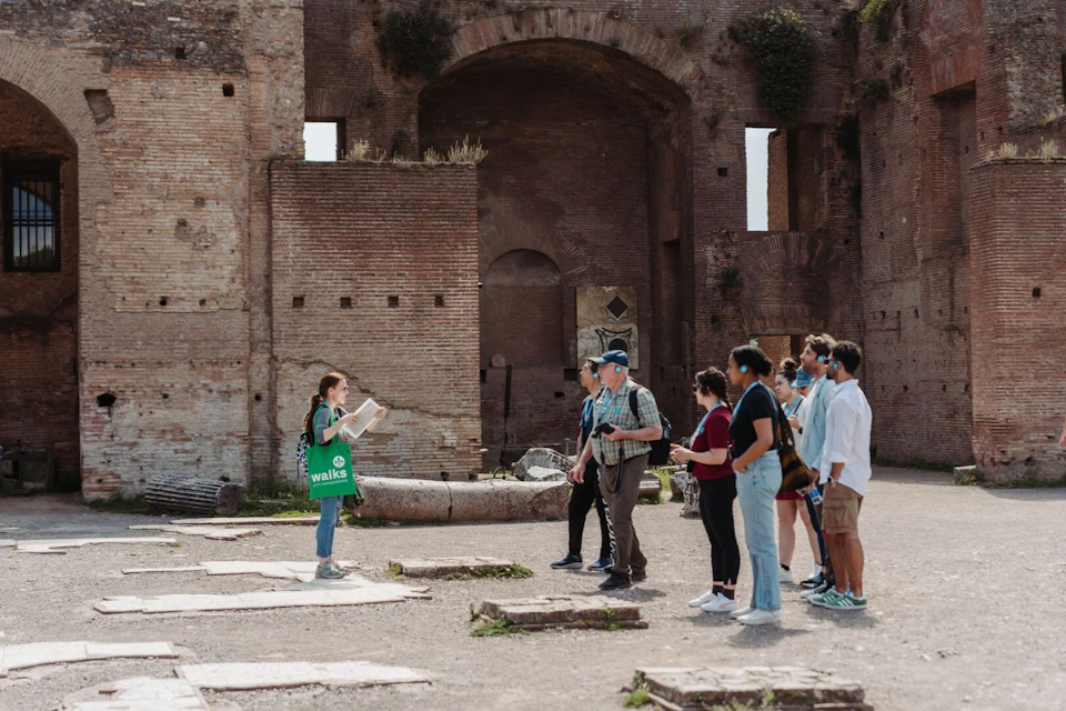 A guide speaks to a group of tourists in an ancient brick ruin. The group listens attentively while standing in the open area.