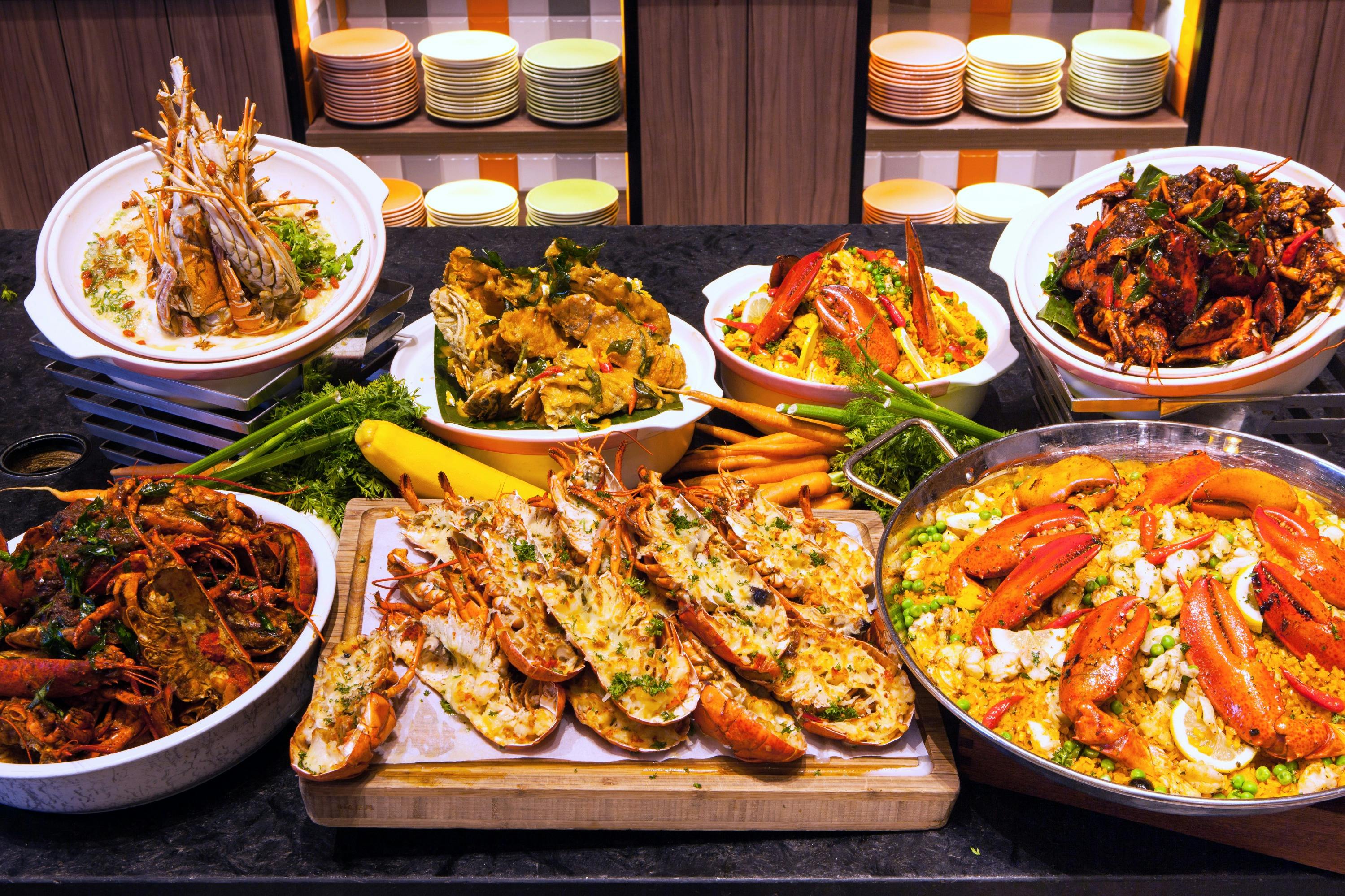 A buffet spread displaying lobster, crab, and other seafood dishes, with colorful plates in the background.