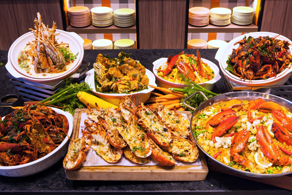 A buffet spread displaying lobster, crab, and other seafood dishes, with colorful plates in the background.