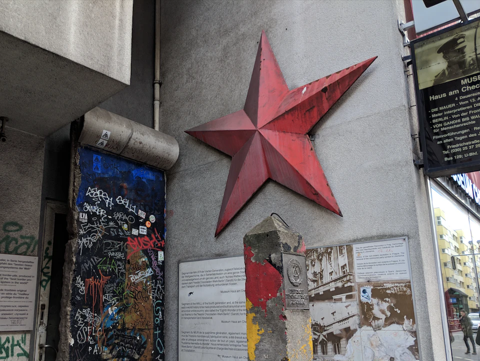 Large red star on a gray wall, colorful graffiti on an adjacent surface, and a weathered monument with informational plaques.