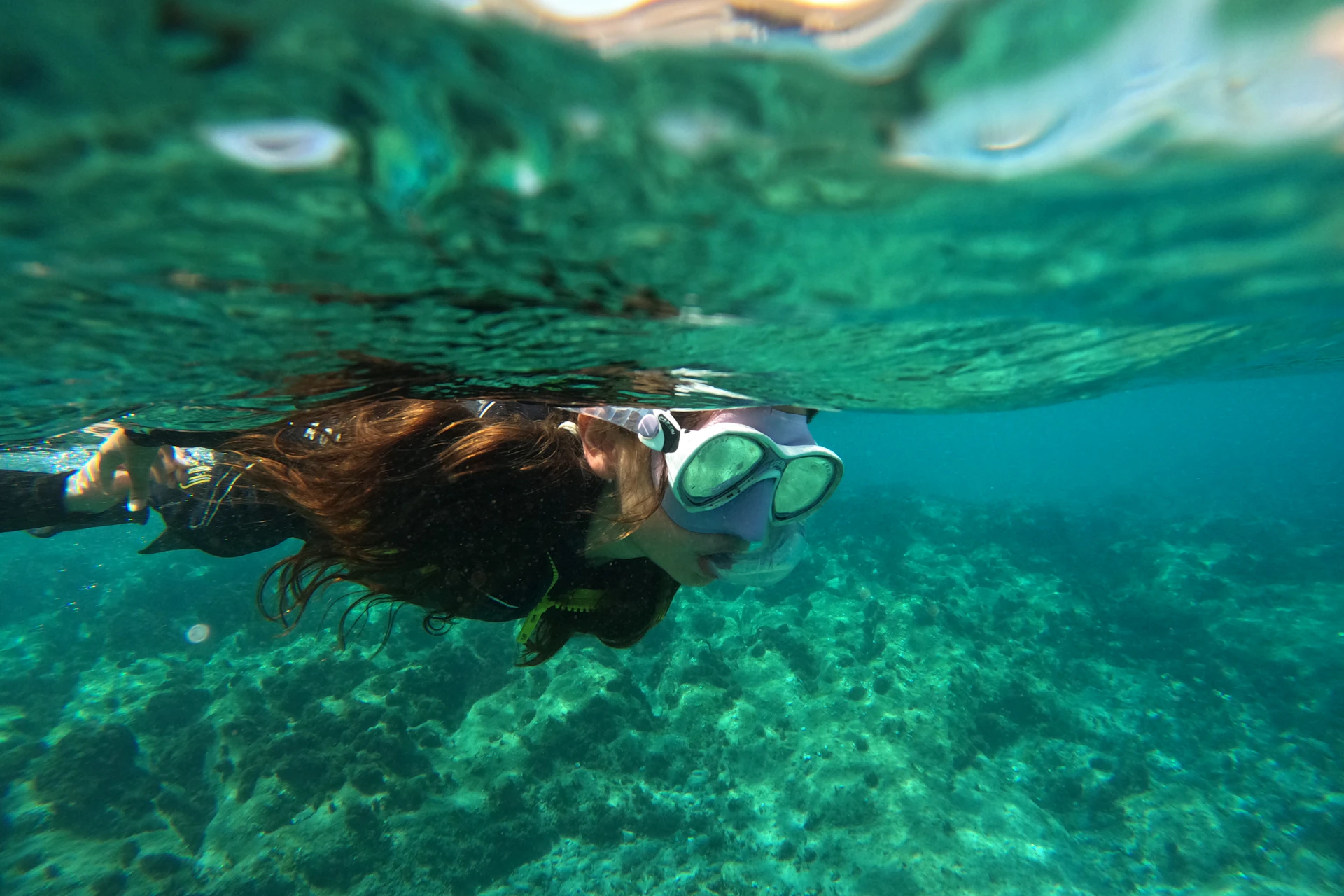 Person snorkeling underwater with clear visibility of coral and seafloor, wearing a mask and snorkel.