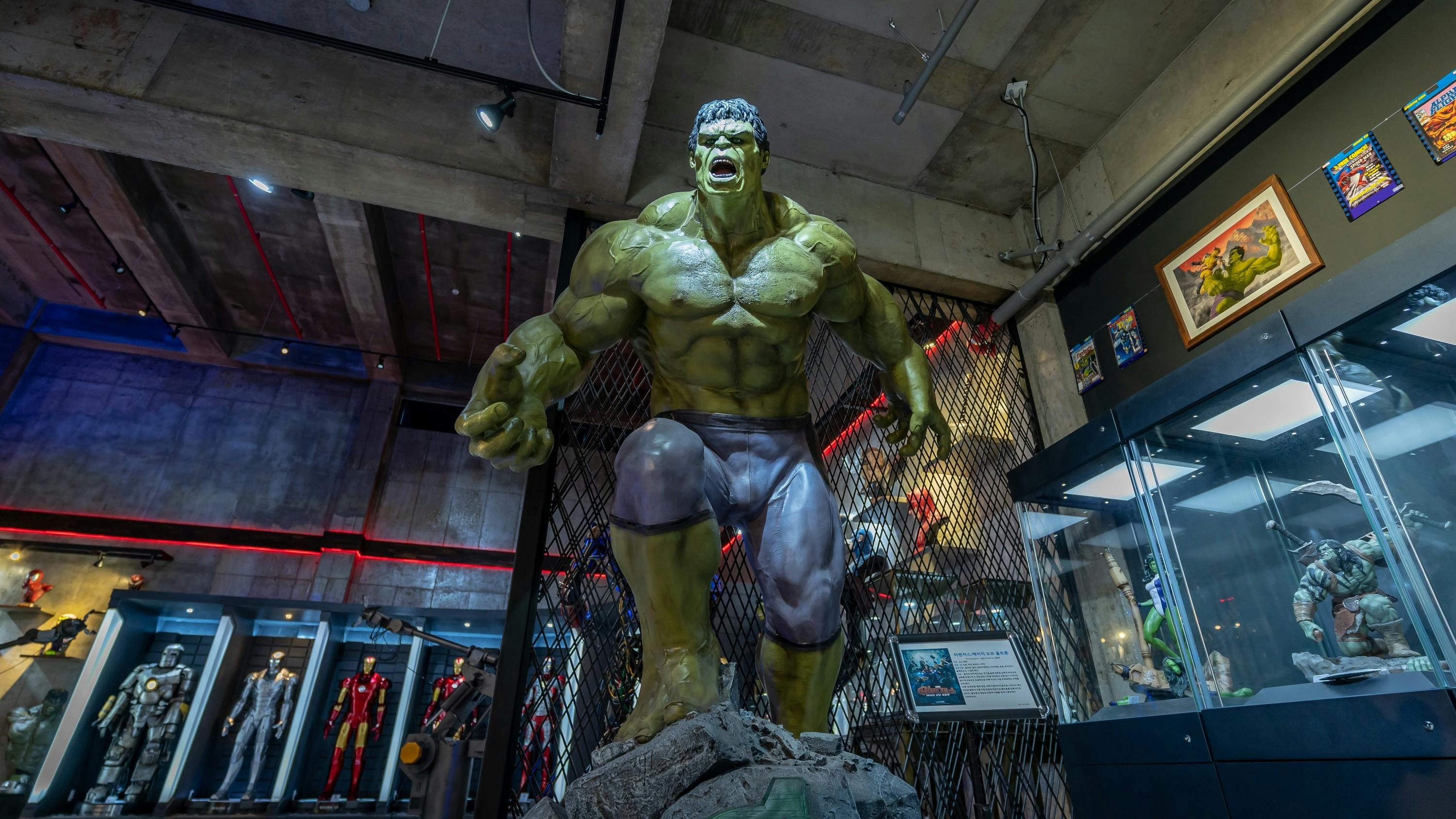 A large statue of a muscular green figure on a rock base, displayed in a museum-like setting with other exhibits.