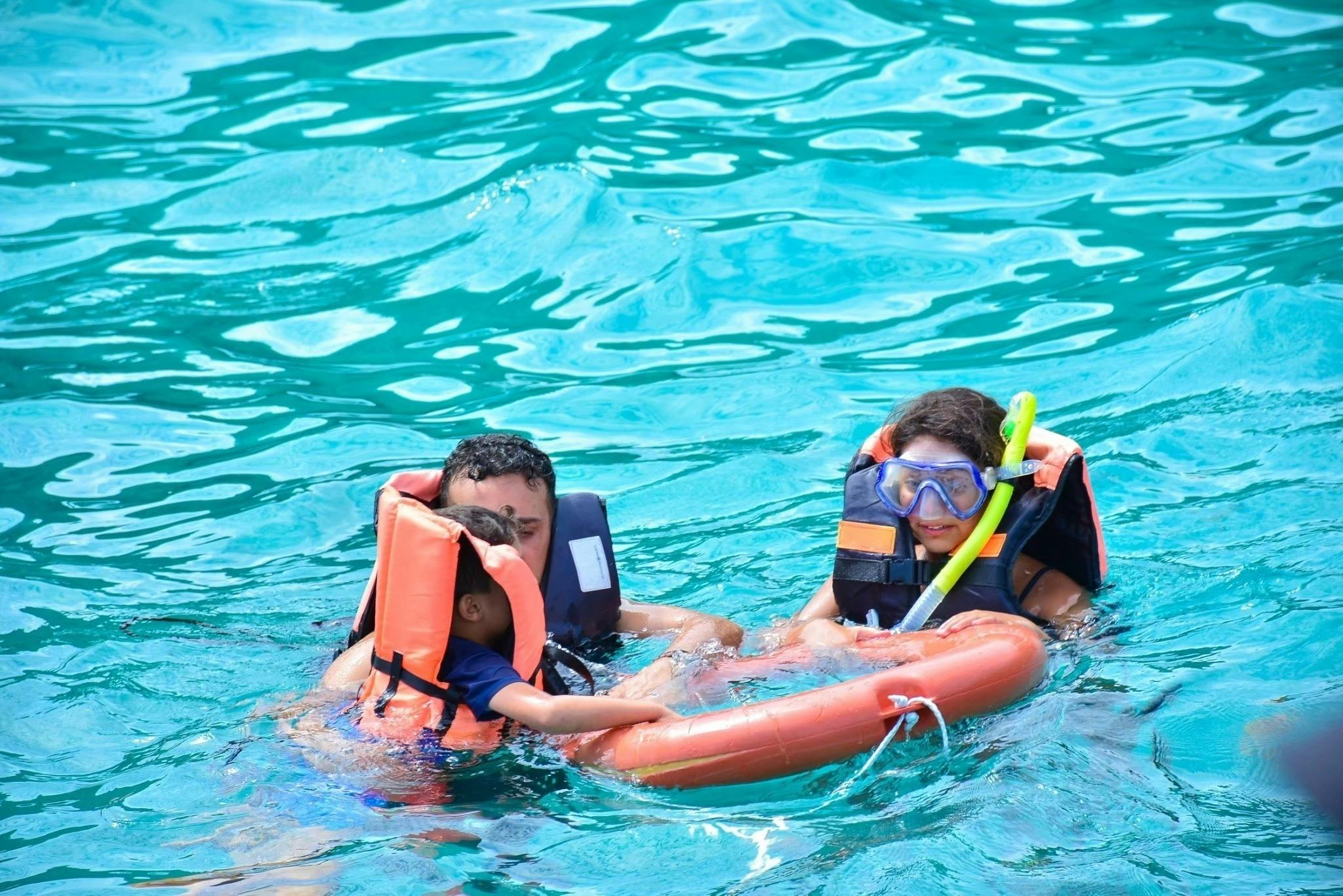 三个穿着救生衣和浮潜装备的人在清澈的绿松石水中游泳，一个拿着橙色漂浮装置。