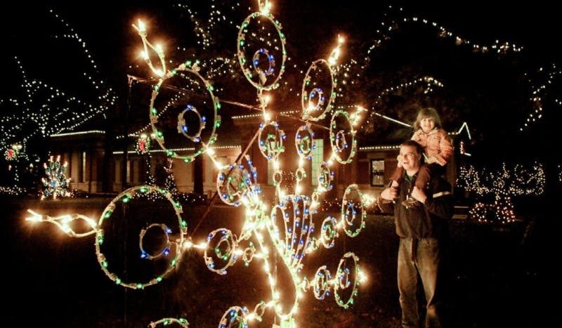 一个肩膀上扛着孩子的男人晚上被节日五彩缤纷的节日灯光包围着。