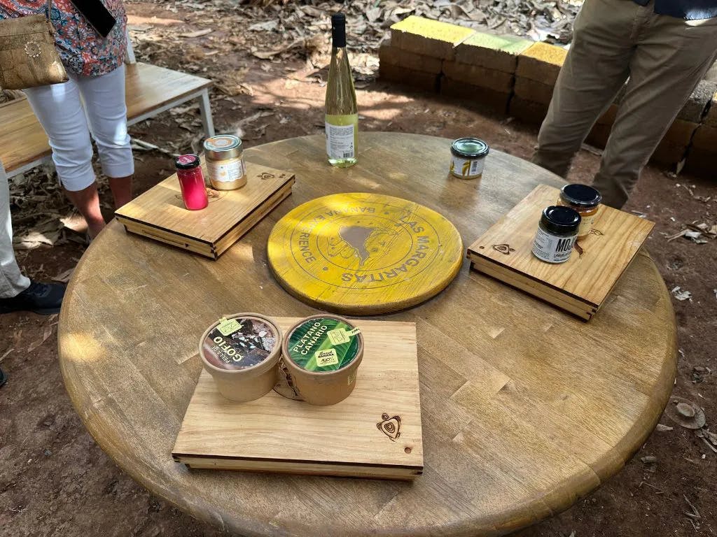 丸い木製のテーブル。木製のトレイには、ワイン、瓶、食料品が置かれています。 テーブルの近くに立っている、部分的に見える2人。