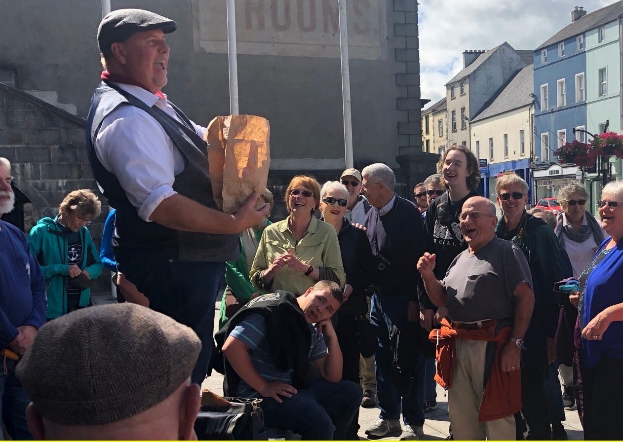 A man with a paper bag entertains an amused crowd outdoors in a town square.