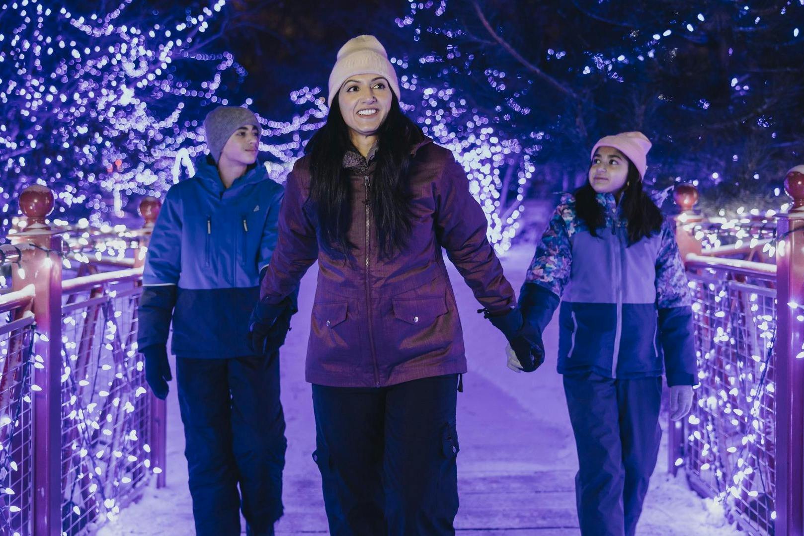 겨울옷을 입은 세 사람이 밤에 파란색과 흰색의 연말연시 조명으로 장식된 길을 따라 걷고 있습니다.