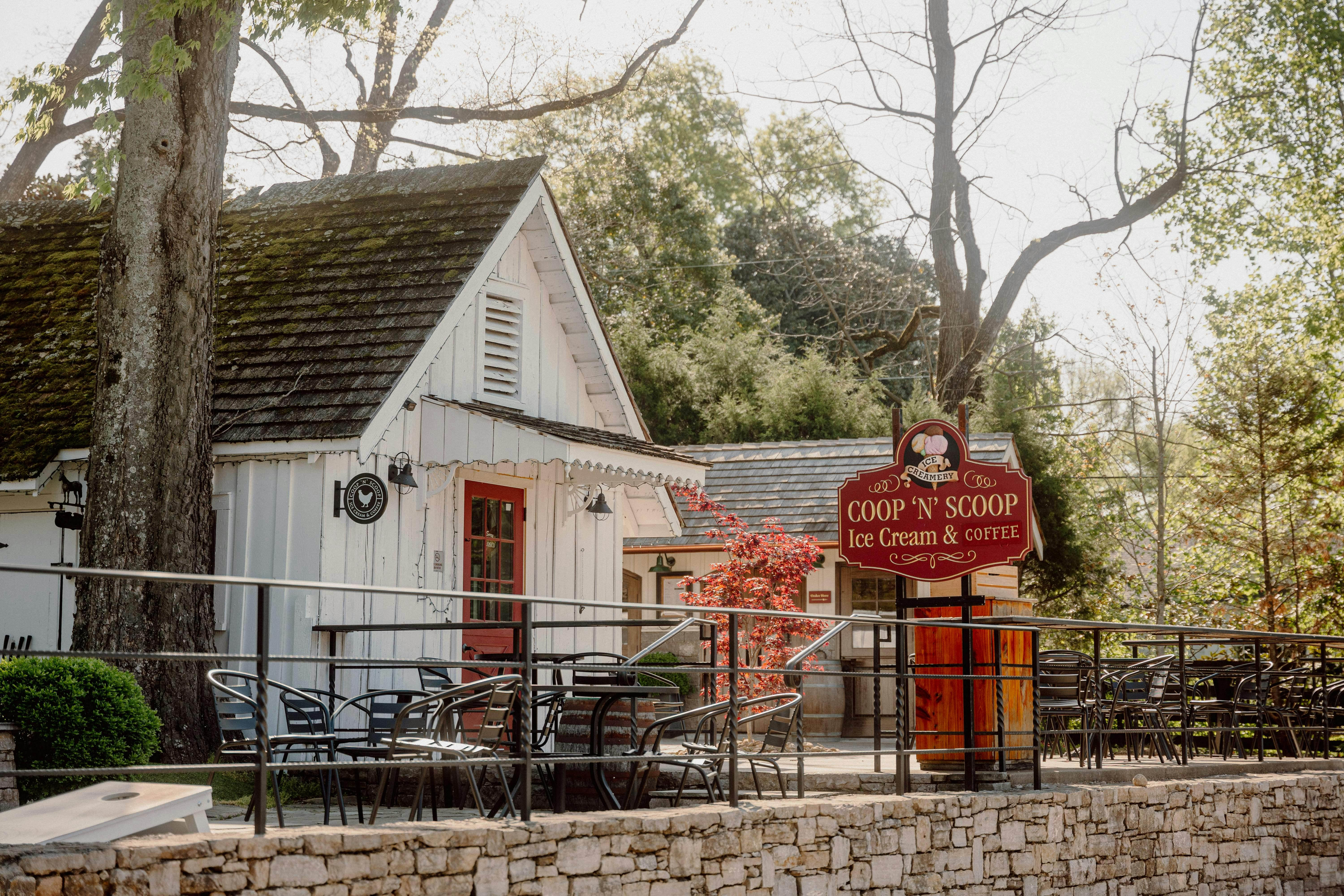 Malebná budova s cedulí „COOP 'N' SCOOP Ice Cream & Coffee“, venkovním posezením a stromy v pozadí.