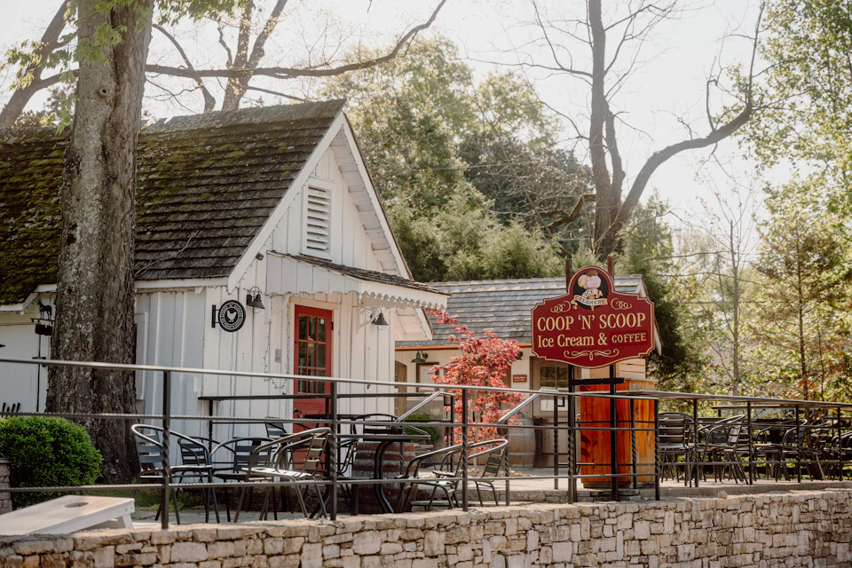 A quaint building with a sign reading "COOP 'N' SCOOP Ice Cream & Coffee," outdoor seating, and trees in the background.
