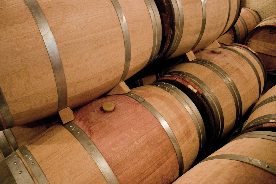 Wooden barrels with metal hoops stacked in a storage area, probably for ageing wine or spirits.