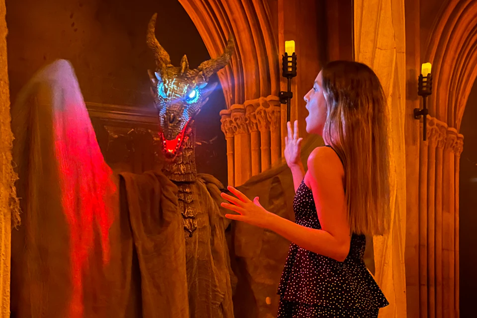 A person reacts to a dragon-like figure with glowing blue eyes in a dimly lit setting with arched architecture.