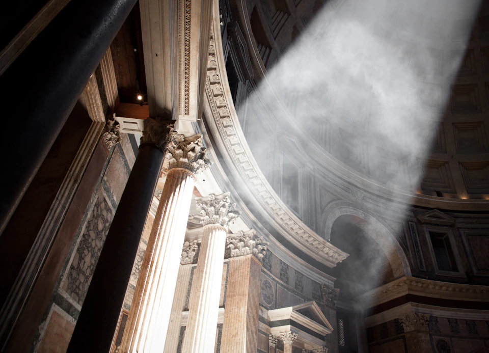 Sunlight streams through the dome, illuminating ornate columns and architectural details inside an ancient building.
