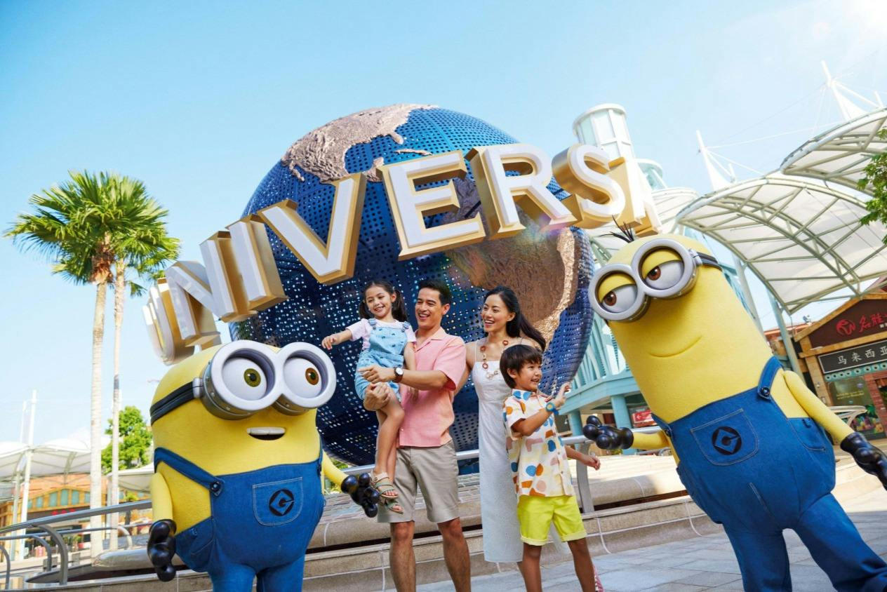 A family poses with two Minion characters in front of a Universal globe sculpture under a clear sky.