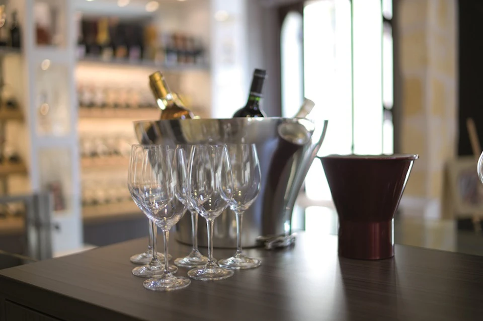 Champagne bottles in an ice bucket, six empty wine glasses, and a decanter on a worktop in a wine shop.
