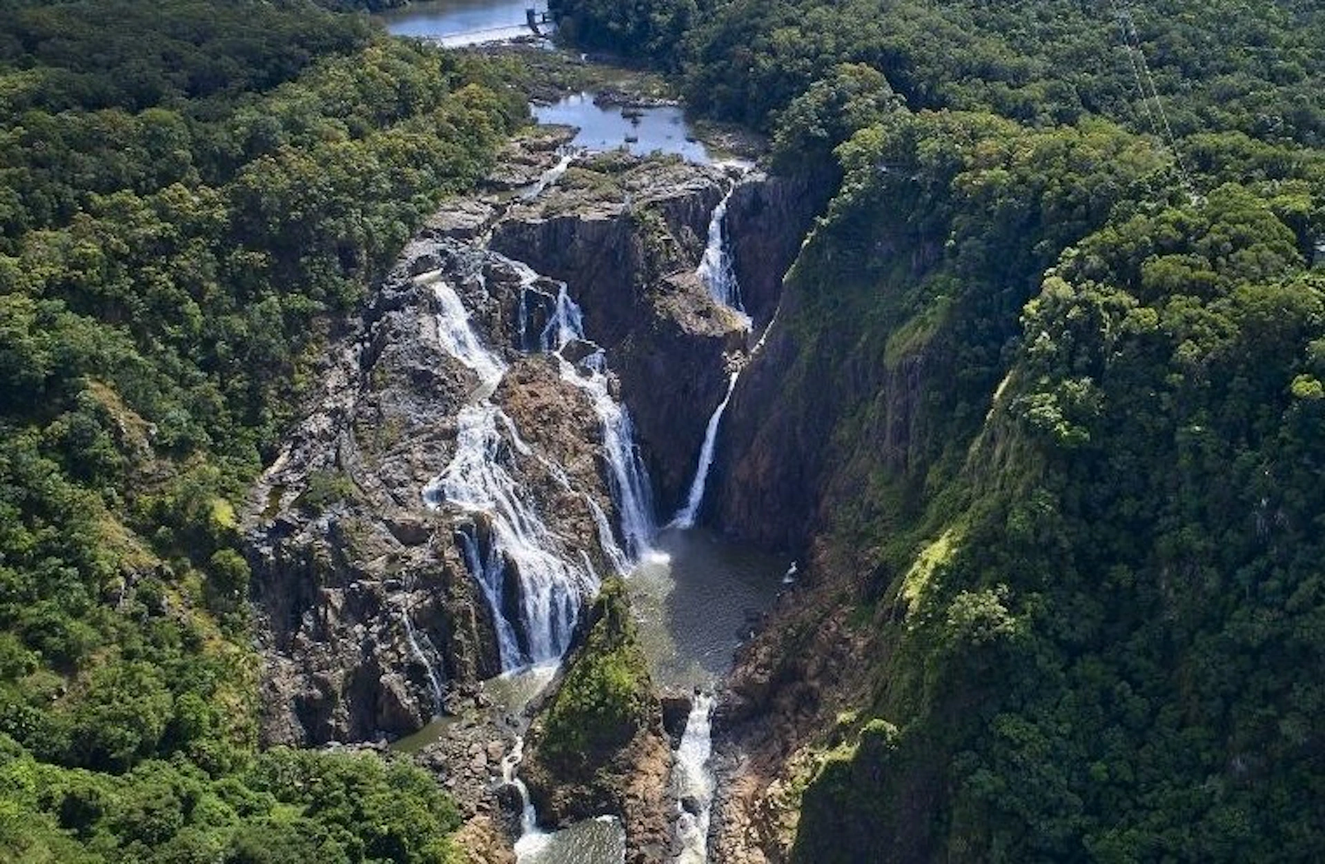 Aerial view of a series of waterfalls cascading down a rocky cliff surrounded by lush green forest.
